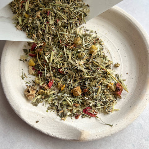 Herbal tea leaves being poured into a white bowl on a light gray background